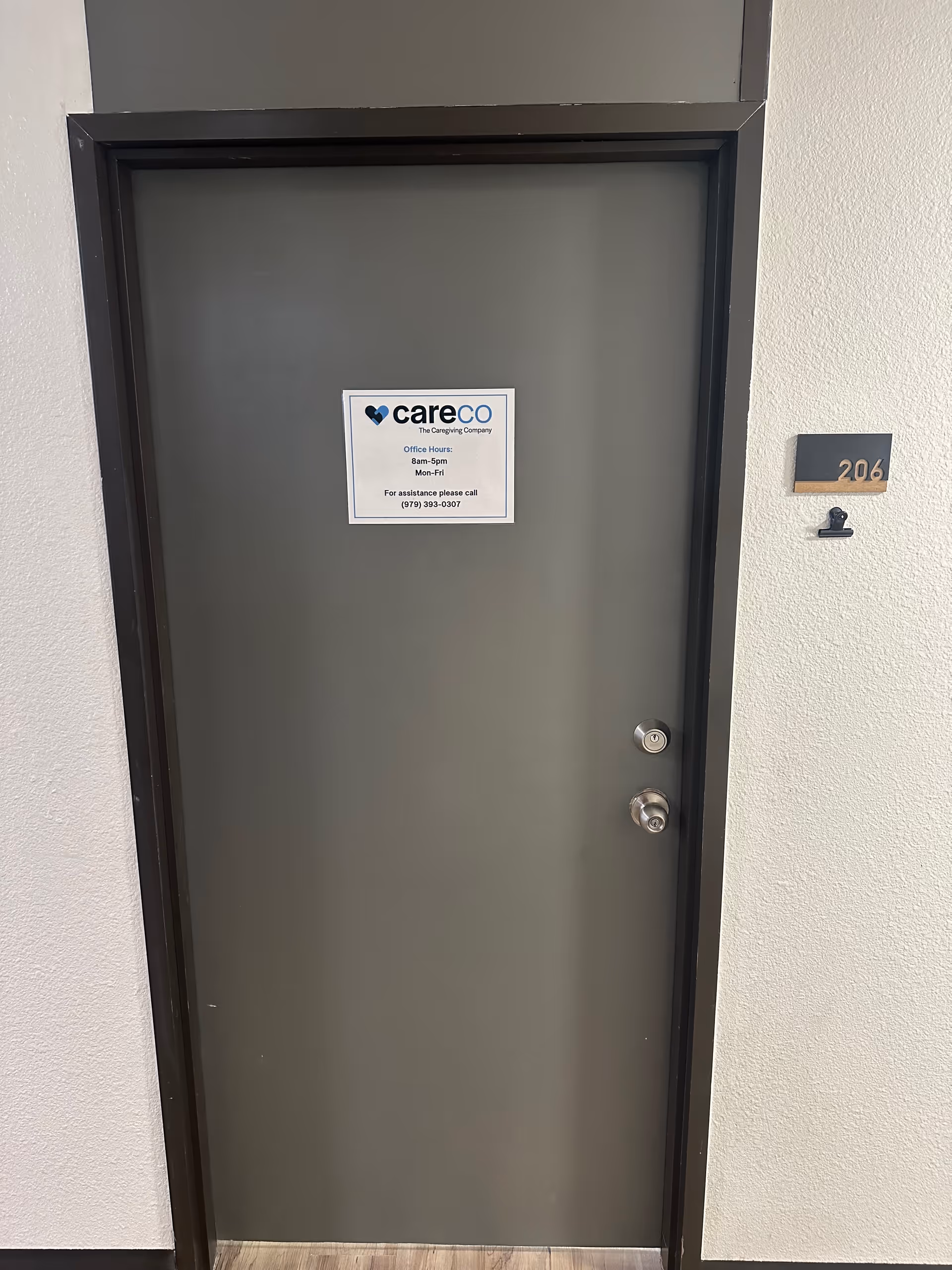 Grey apartment door with CareCo sign and unit number 206 in a beige hallway.