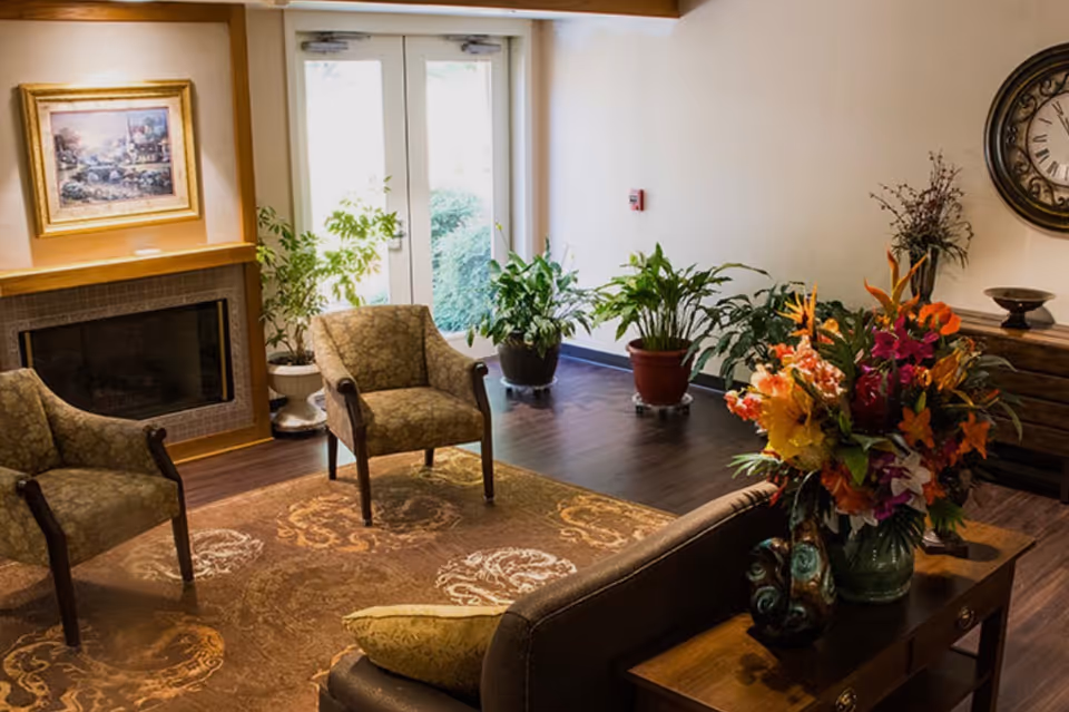 Cozy living room with chairs, fireplace, plants, and a vibrant flower arrangement.