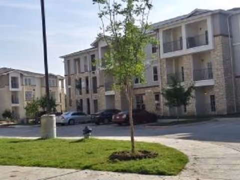Exterior view of a multi-story senior living building with parking, trees, and landscaping.