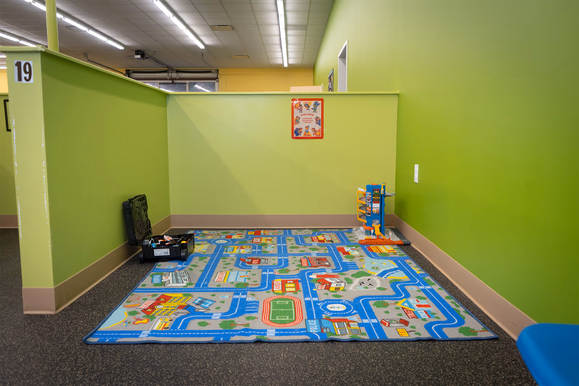 Bright green walls enclose a children's play area with a colorful city rug and toys.