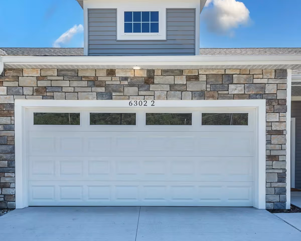 Stone facade exterior with a large white garage door and clear blue sky.