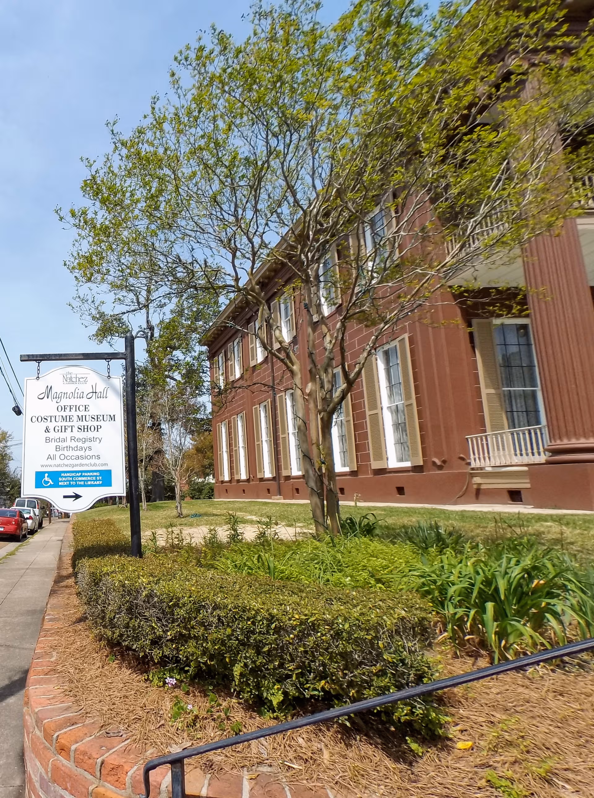 Brick building facade with trees, hedges, and a sidewalk sign for Magnolia Hall.