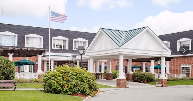 Prescott House senior living facility exterior with brick building, covered entrance, flag, and landscaping.