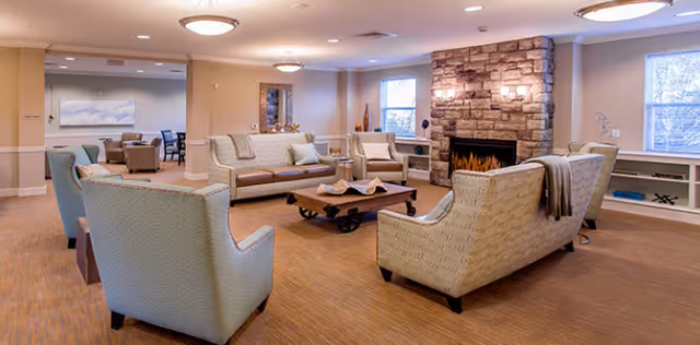 Cozy senior living lounge with sofas, armchairs, a coffee table, and a stone fireplace.