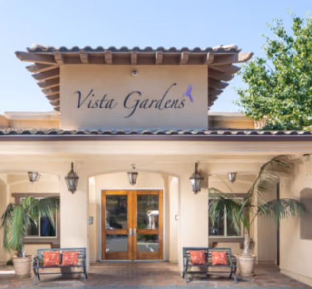 Vista Gardens memory care facility front entrance with double wooden doors and potted palm plants.