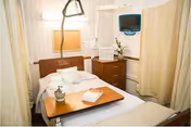 Hospital-style resident room with bed, privacy curtains, dresser, and medical monitor.