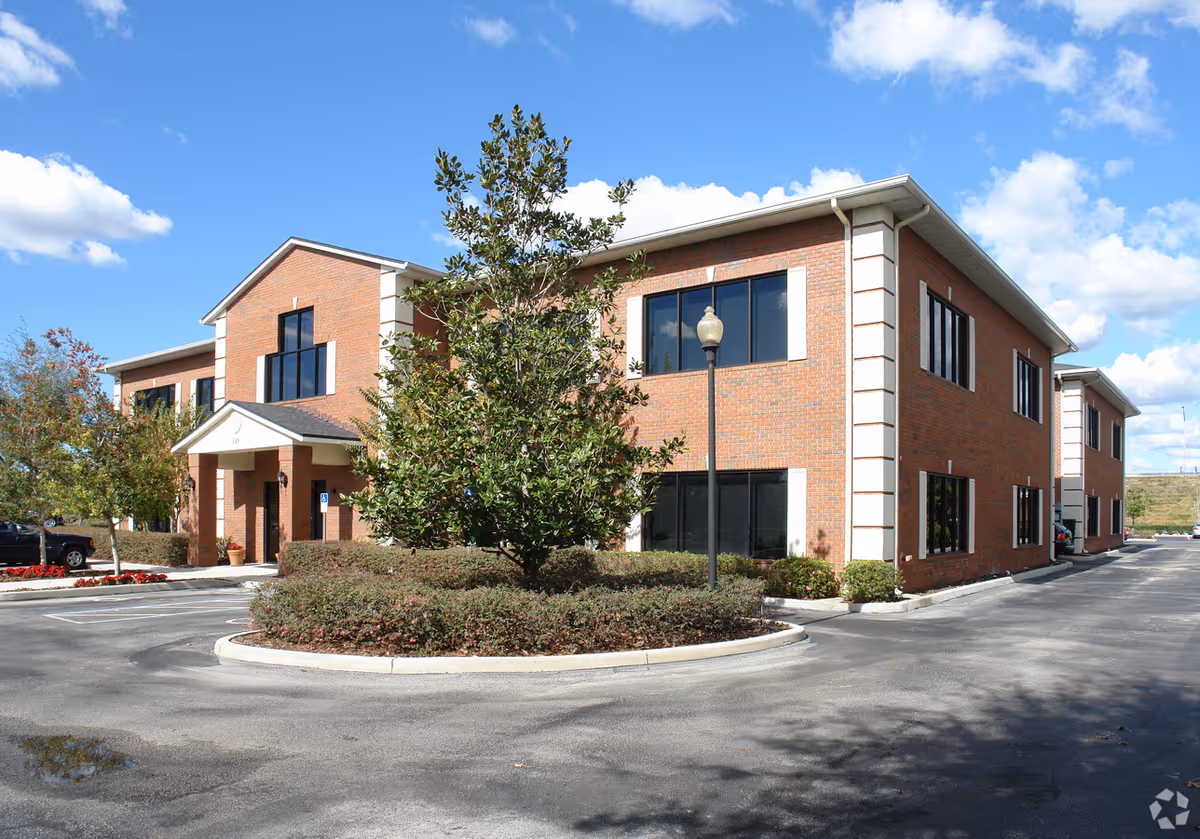 Two-story brick senior living facility with parking, landscaping, and blue sky.