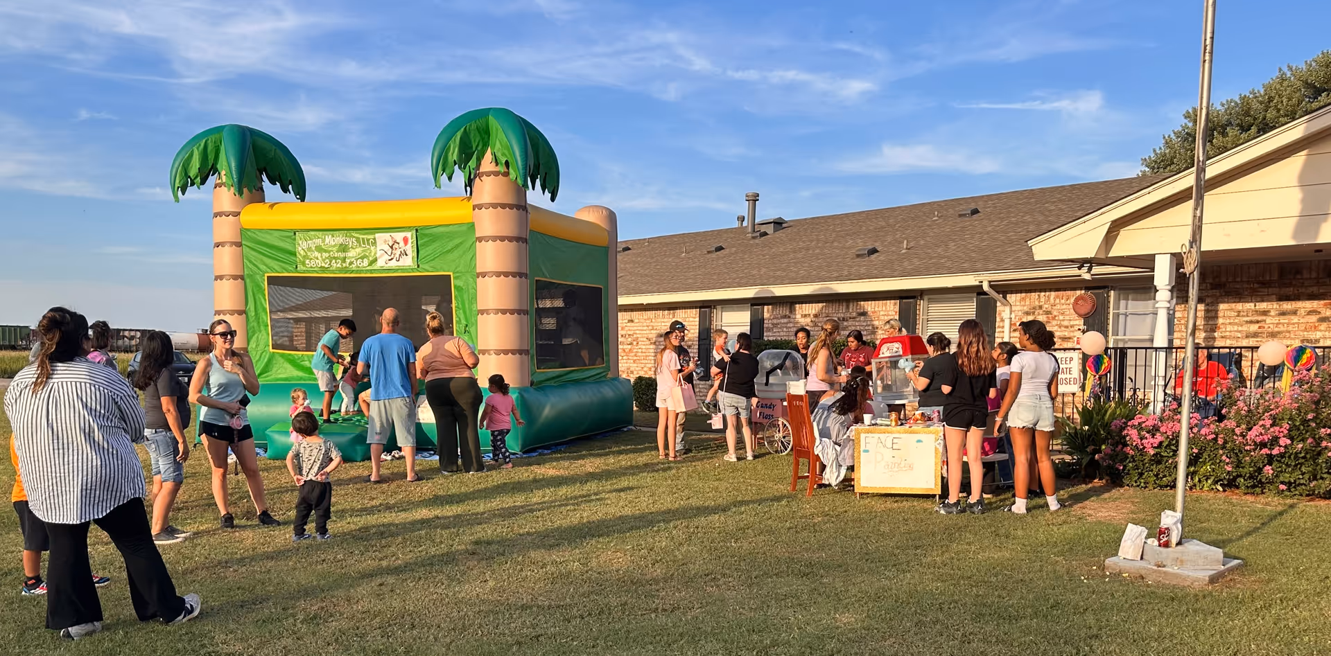 Outdoor community event at The Living Center features a palm-tree inflatable bounce house and attendees.