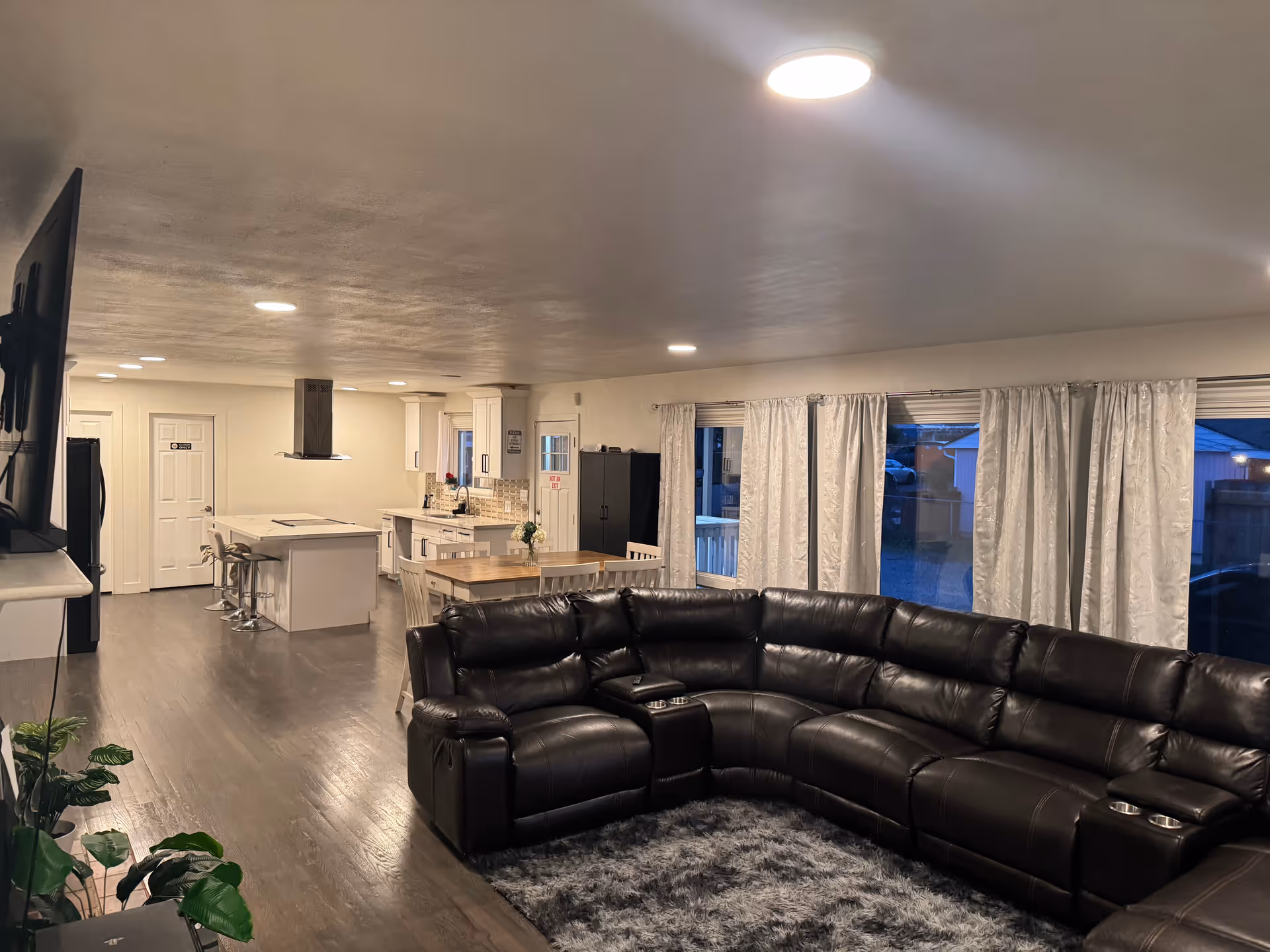 Open-concept living area with black leather sectional, kitchen island, and dining table.