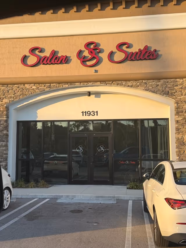 Exterior view of a Salon & Suites building with glass doors and parked cars.