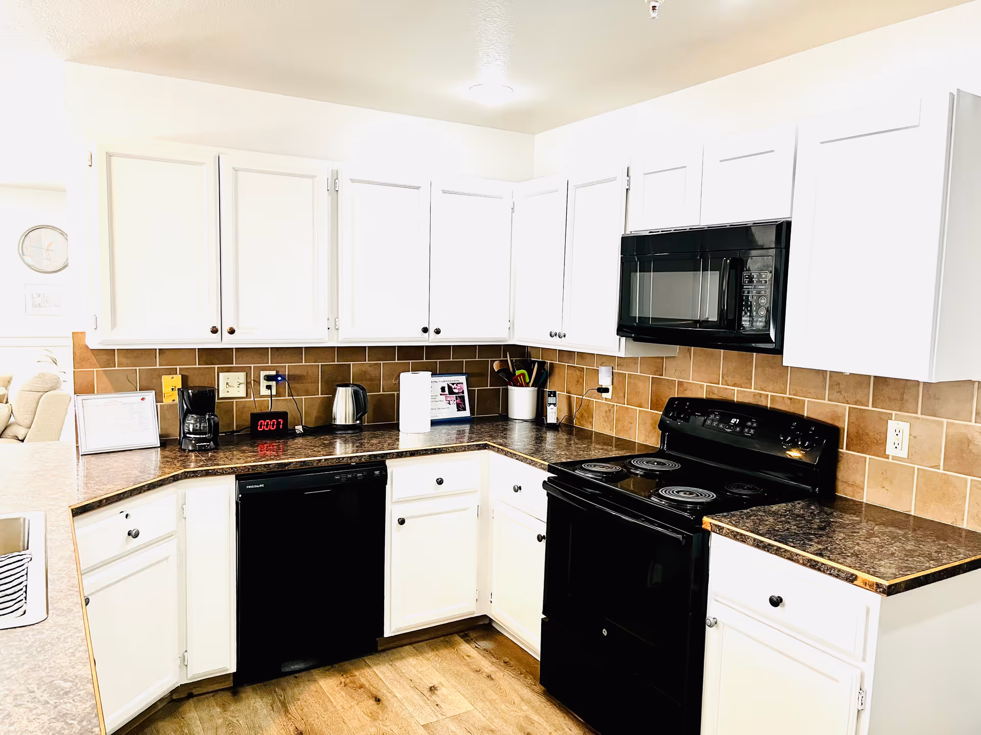 White kitchen with brown tile backsplash, black appliances, and white cabinets in an L-shaped layout.