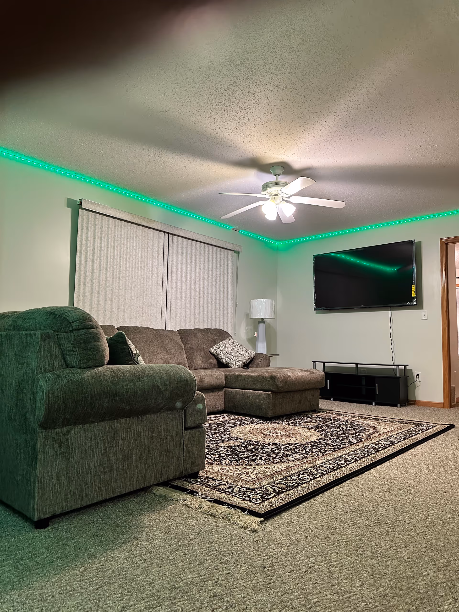 Cozy living room in a senior living facility with green LED lighting, sofa, rug, and TV.