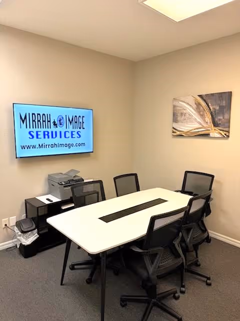 Conference room with a white table, six chairs, wall-mounted display, and artwork.