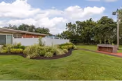 Well-manicured outdoor lawn with shrubs, a brick structure, and a white building in background.