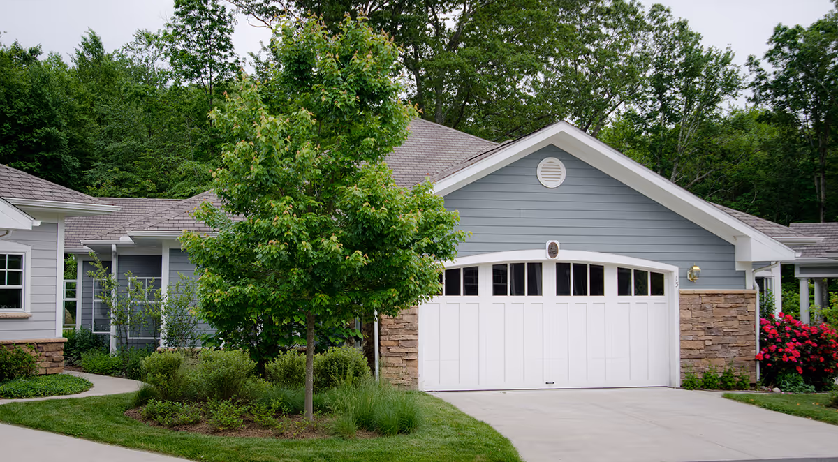 Front exterior of a single-story gray building with a white garage door, landscaped lawn, and trees.