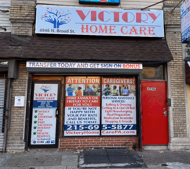 Storefront of Victory Home Care with large sign, red door, and posters