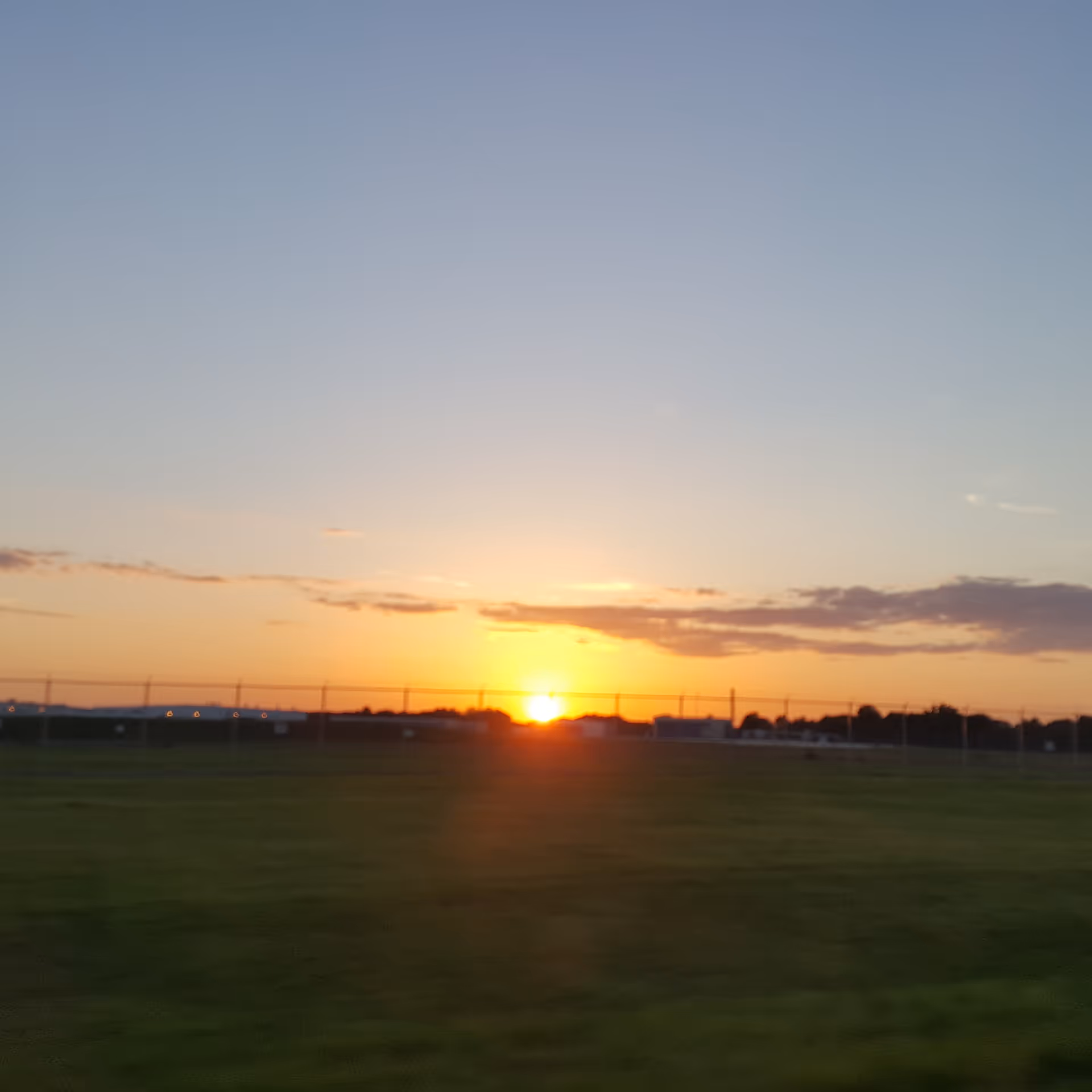 Sunset over a grassy field with distant buildings along the horizon.