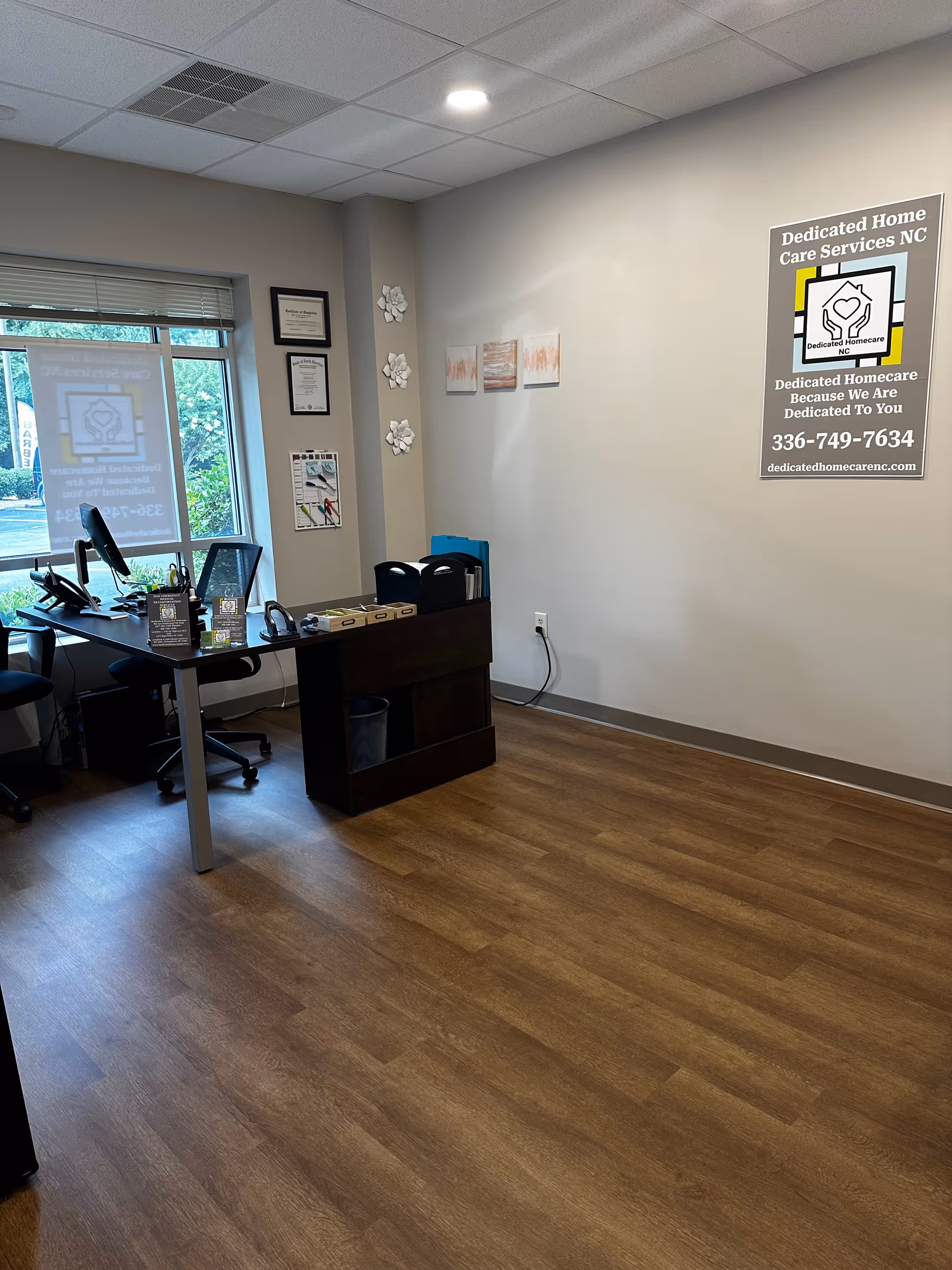 Office reception area with a desk, computer, chairs, and a Dedicated Homecare NC sign.