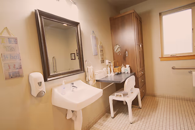 Bathroom with sink, mirror, cabinet, chair, and toiletries in Tuscany Cottage Adult Family Home.