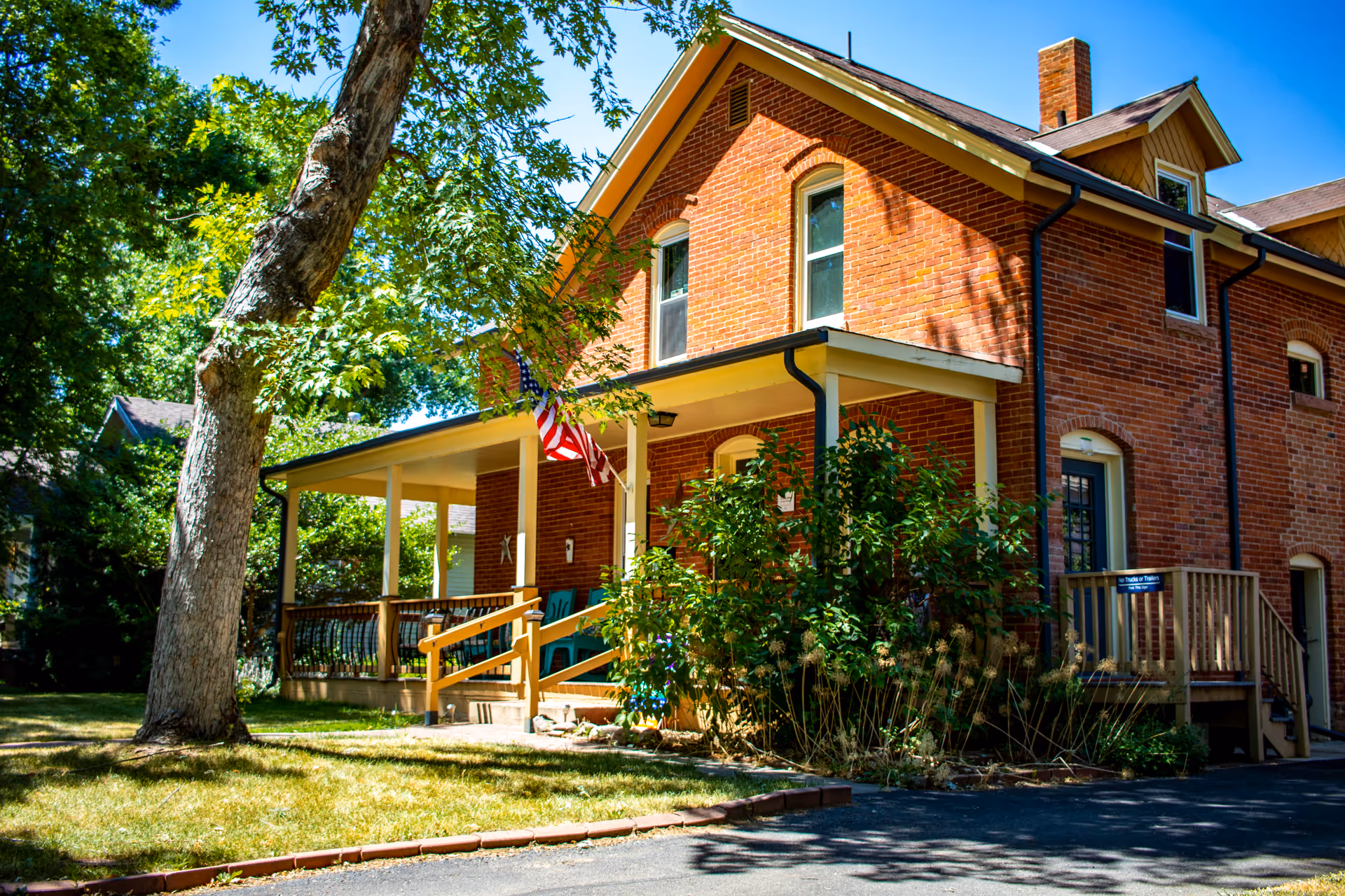 Brick assisted living building with a covered front porch, greenery, and an American flag.