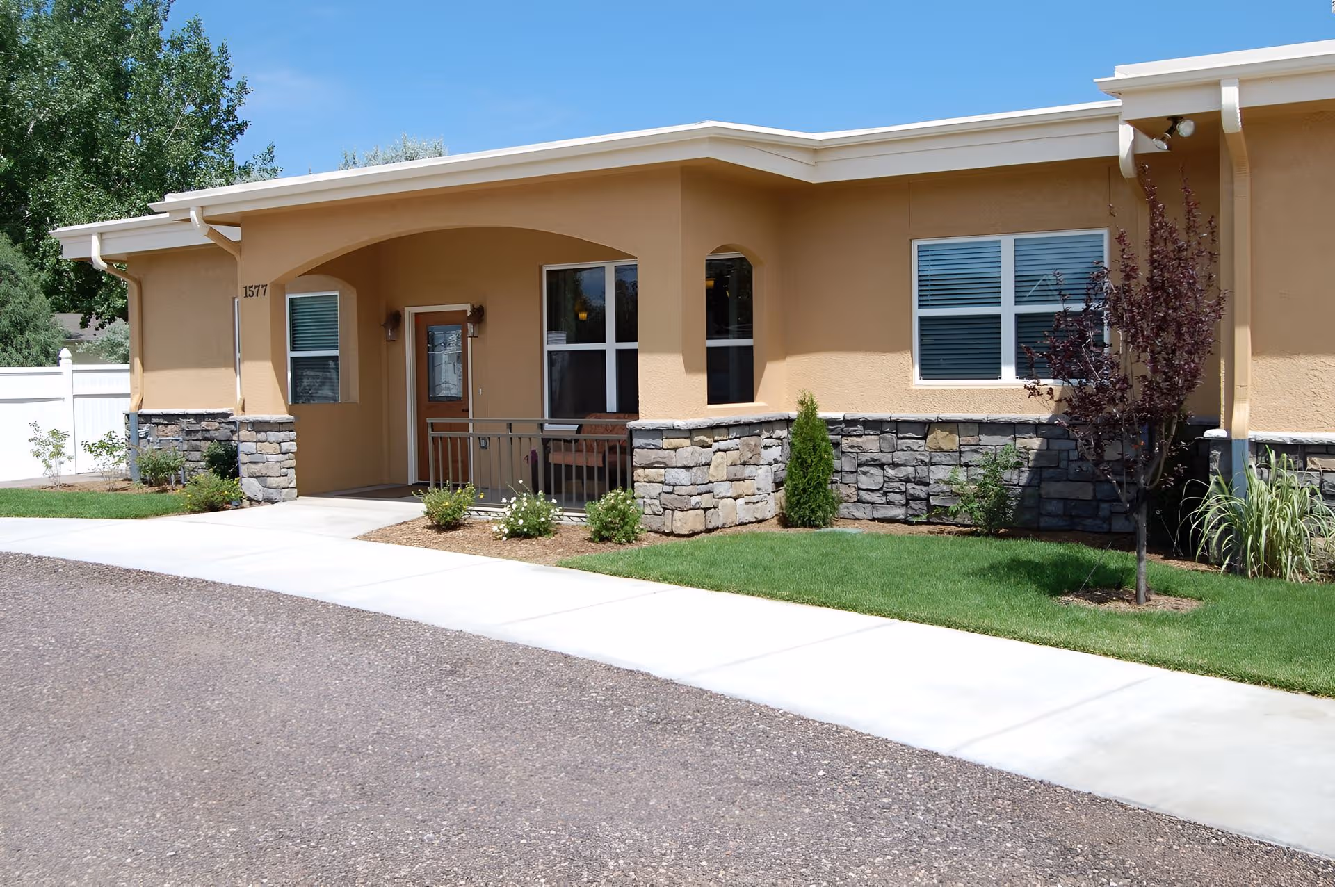 A single-story assisted living facility front with beige stucco and landscaping.