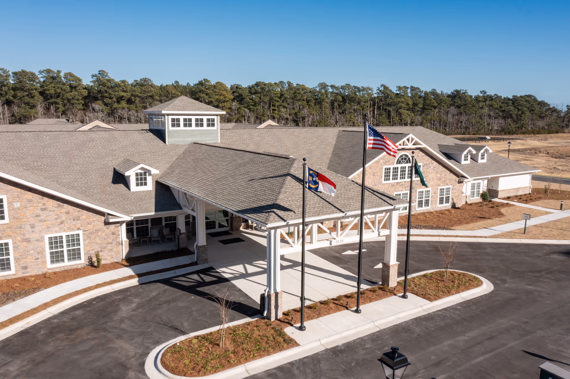 Aerial view of a senior living facility front entrance with flags and parking.