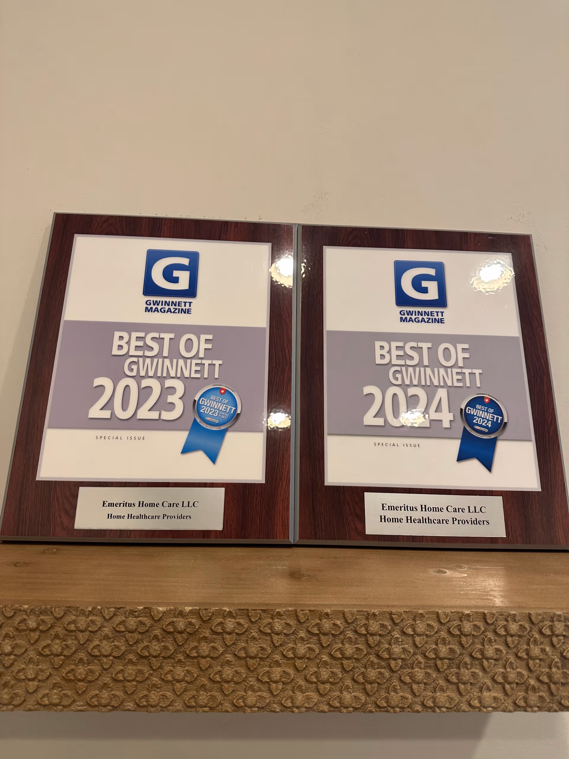 Two framed awards labeled Best of Gwinnett 2023 and 2024 beside Emeritus Home Care LLC plaques.
