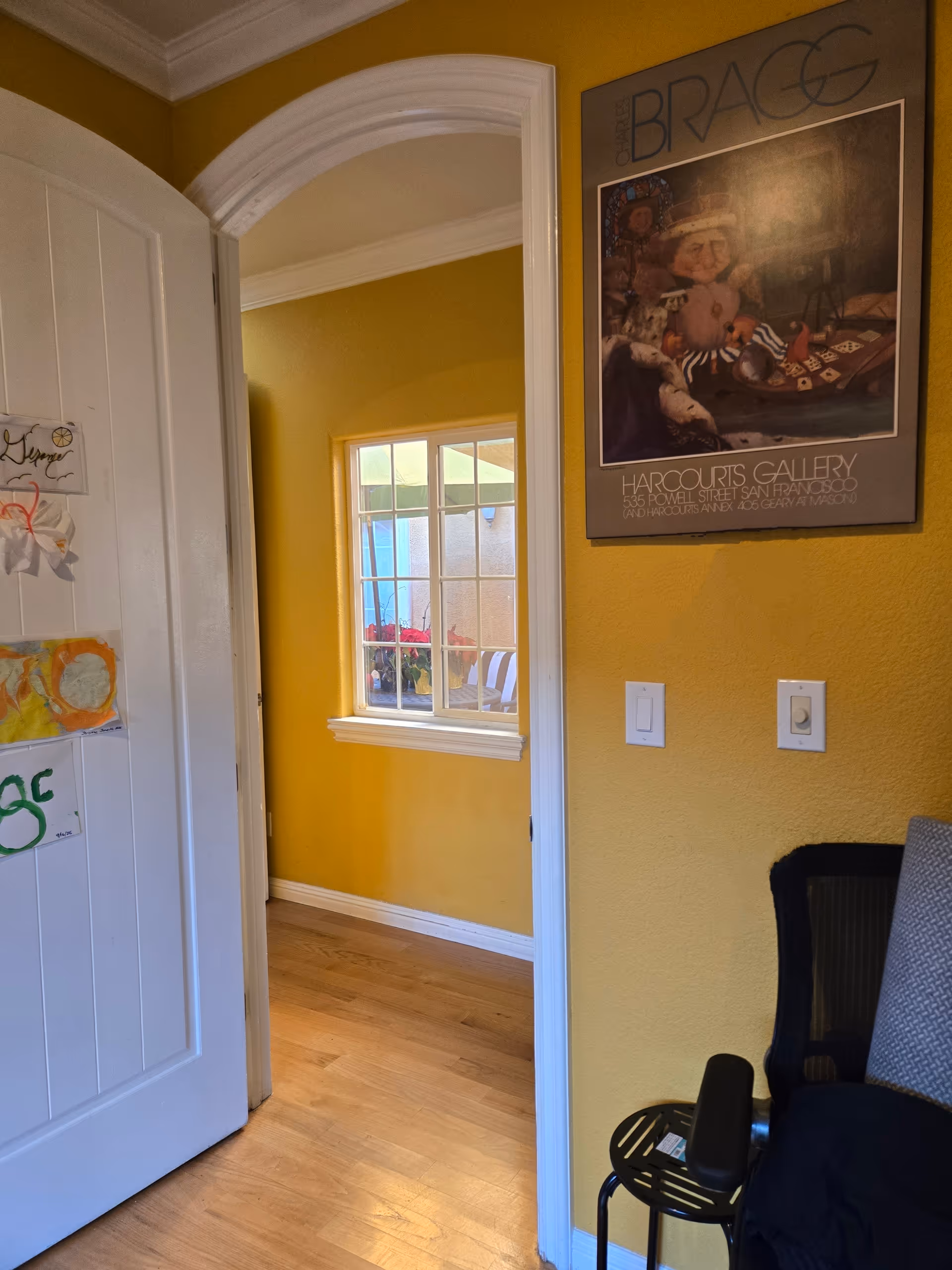Yellow-walled interior hallway with doorway, poster, window view, and a chair