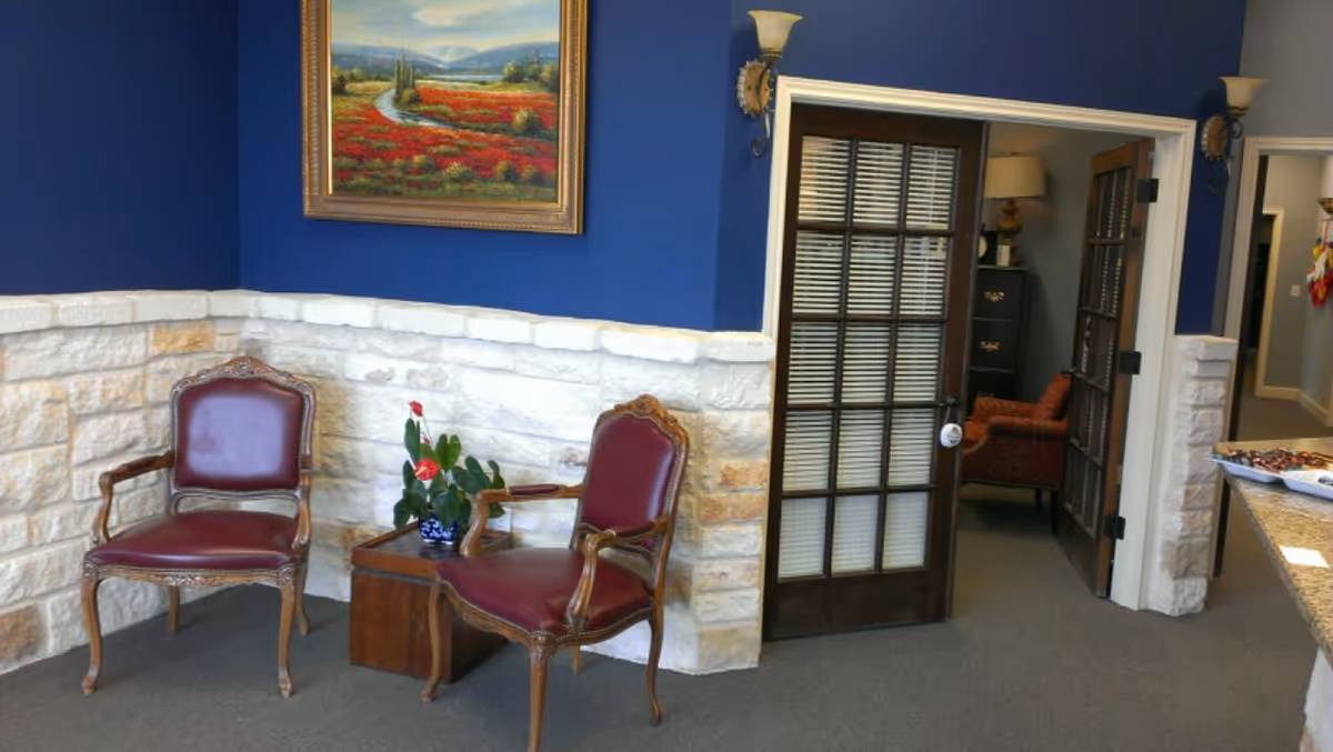 Two red-upholstered chairs flank a small table with a plant in a blue-walled lobby.