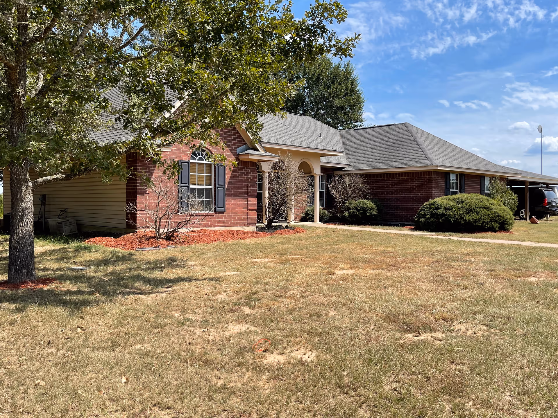 Single-story brick senior living facility exterior with front entrance, trimmed shrubs, and a driveway.