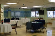 Empty dining room with round tables, chairs, and windows in a senior care facility.