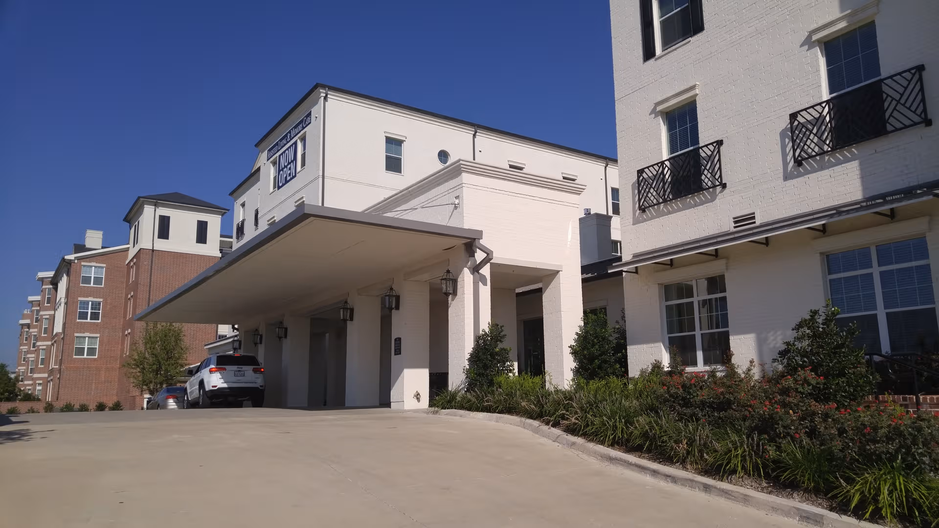 White multi story senior living building with a covered entrance and parked cars.