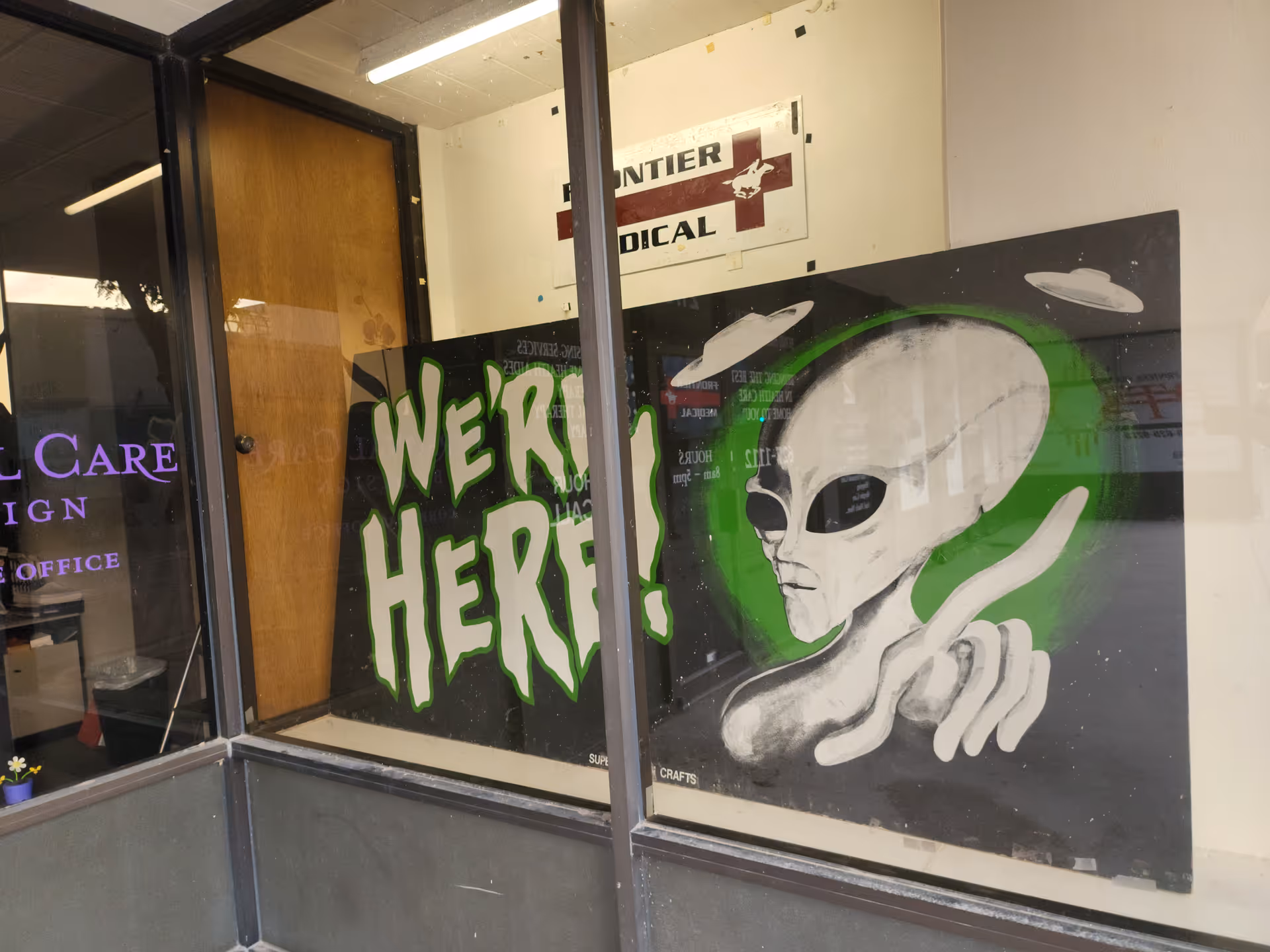 Interior storefront window with graffiti reading WE'RE HERE and Frontier Medical sign