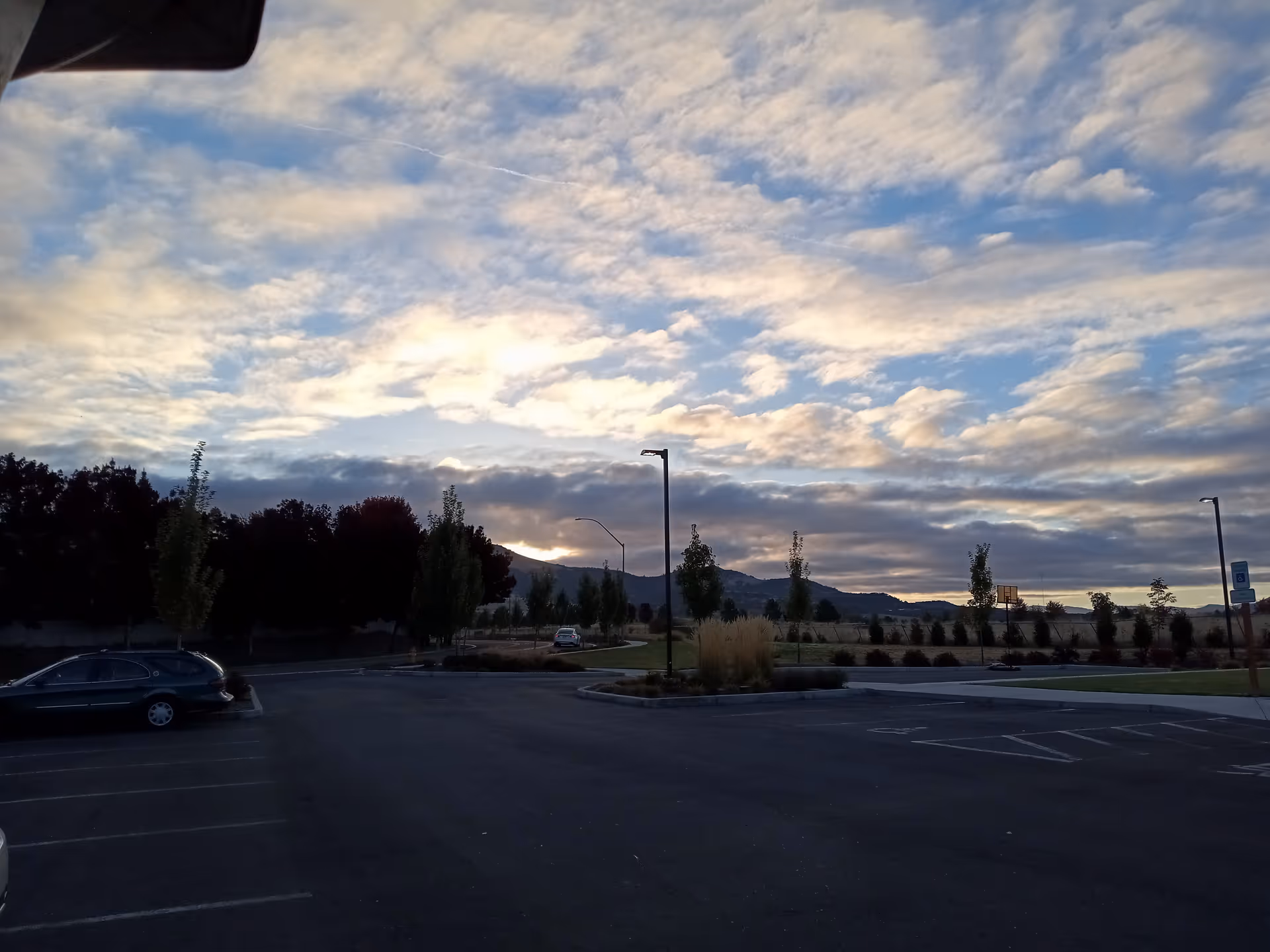 Parking lot foreground with trees and distant mountains under a blue cloudy sky.