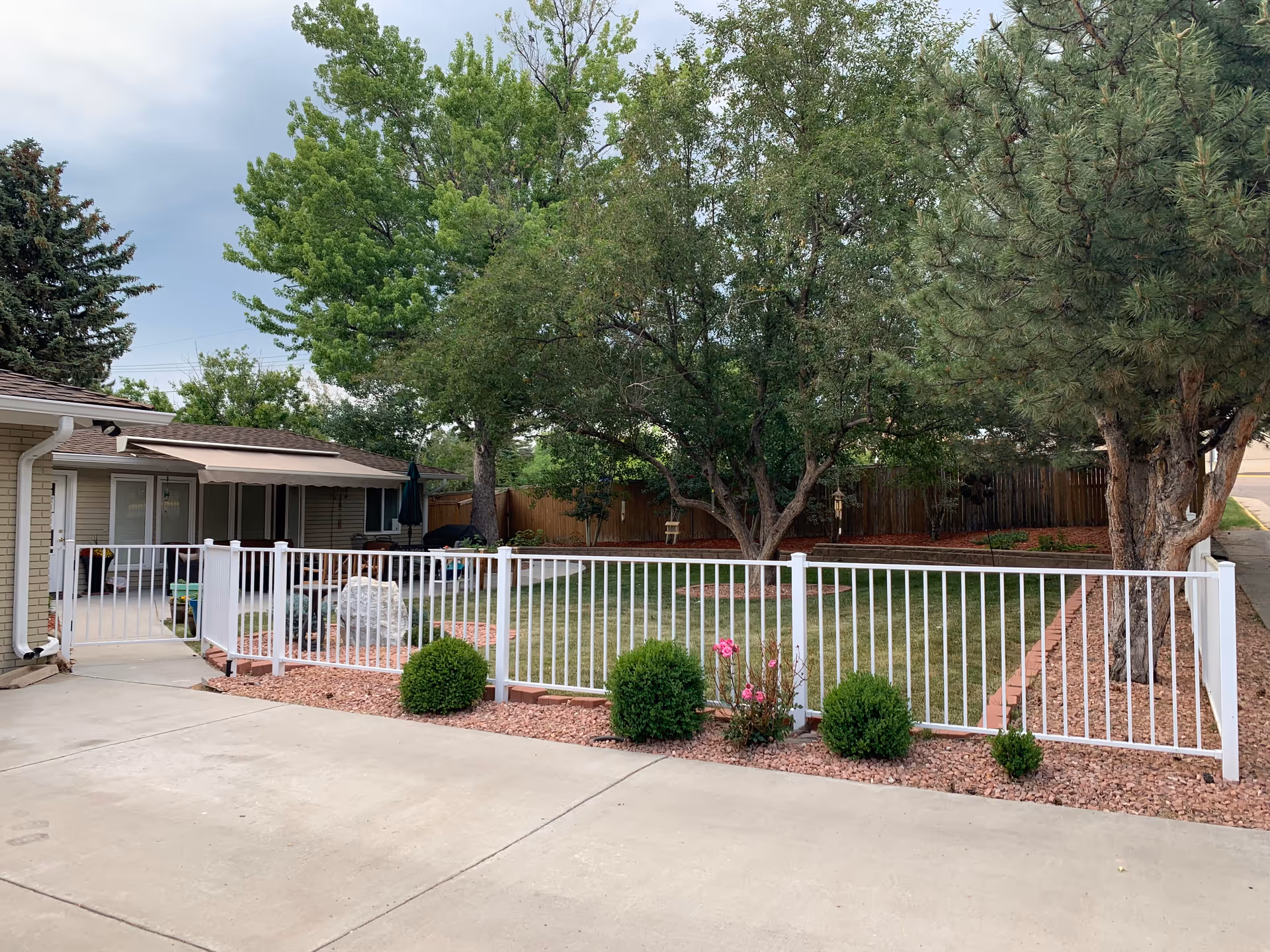 Exterior view of Serenity House Assisted Living with a white fence, trees, and landscaped yard.
