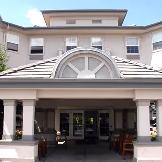 Front entrance of a beige multi-story senior living facility with arched window and columns.