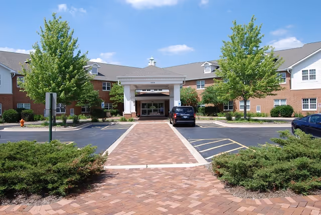 Exterior view of a brick senior living facility entrance with a brick walkway leading to doors.