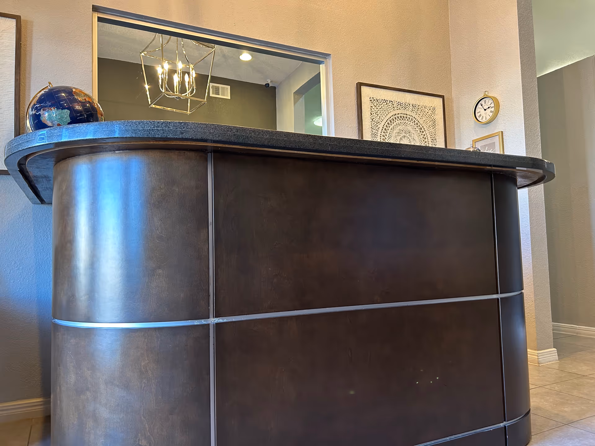 Curved dark reception desk in a lobby with framed art and a clock on the wall.