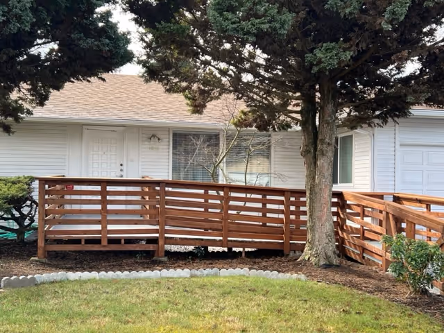 White single-story building with a wooden ramp and a large tree in front.