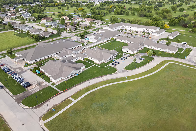 Aerial view of a senior living campus with tan-roofed buildings and green grounds.