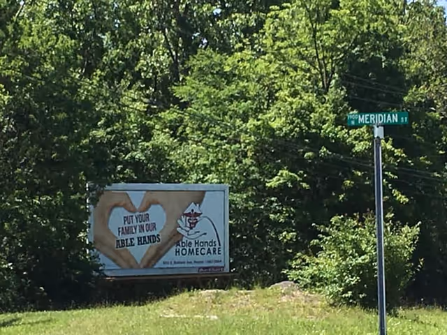 Outdoor roadside billboard for Able Hands Homecare beside trees and greenery.