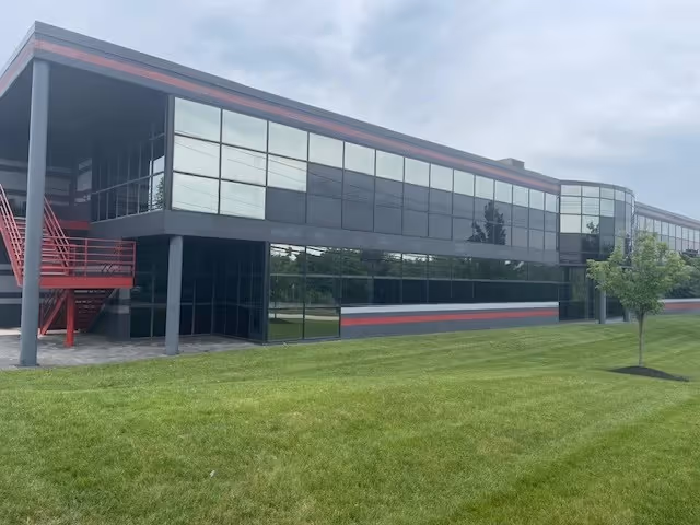 Modern glass-front facility with red exterior stairs, dark siding, and a green manicured lawn.