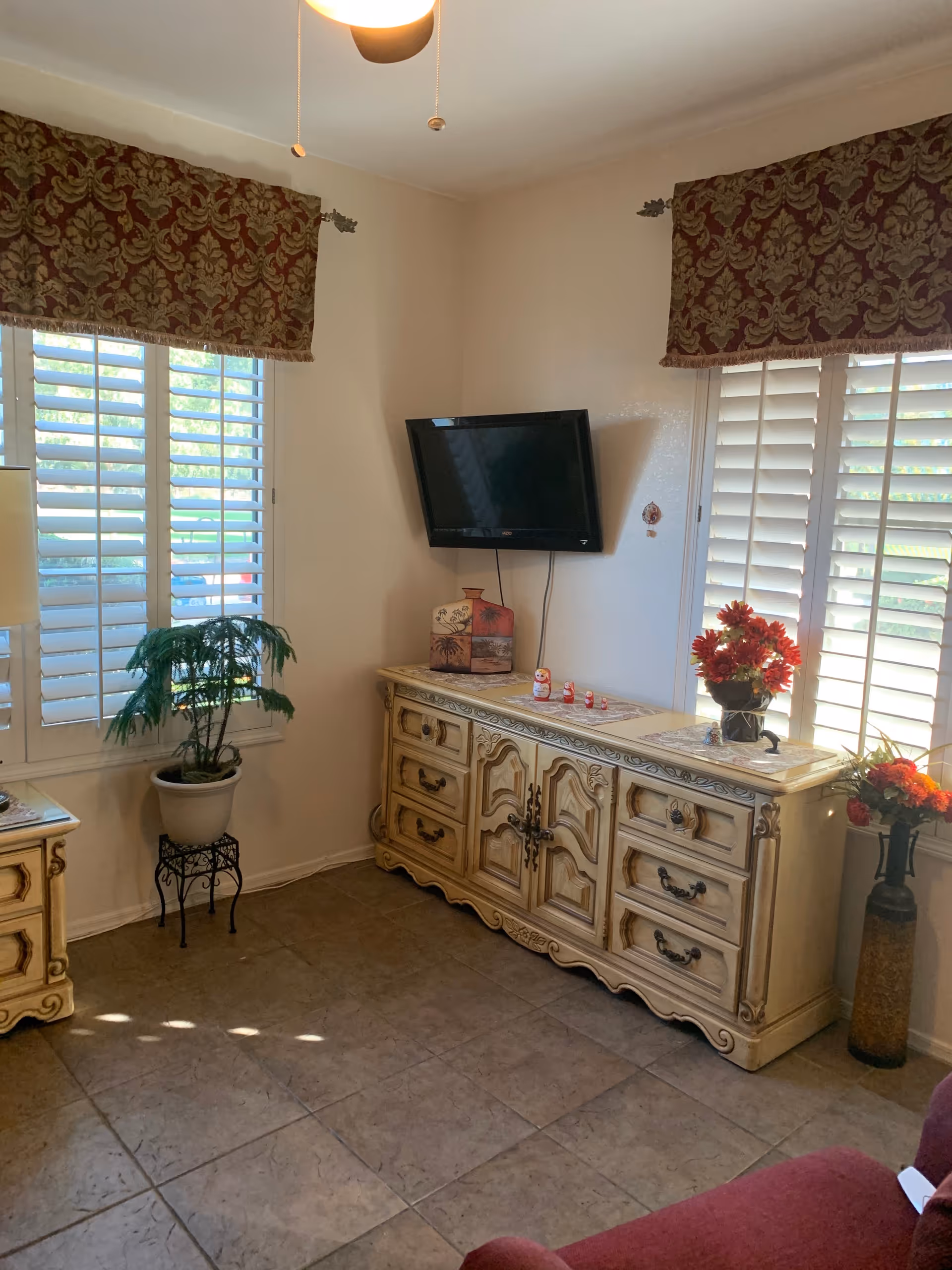 Ornate cream dresser beneath wall-mounted TV in a bright living room with plants.