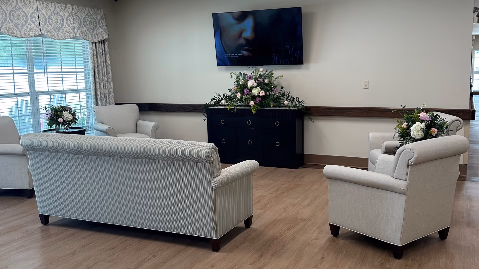Cozy lounge with beige seating, flowers, and a wall-mounted TV.