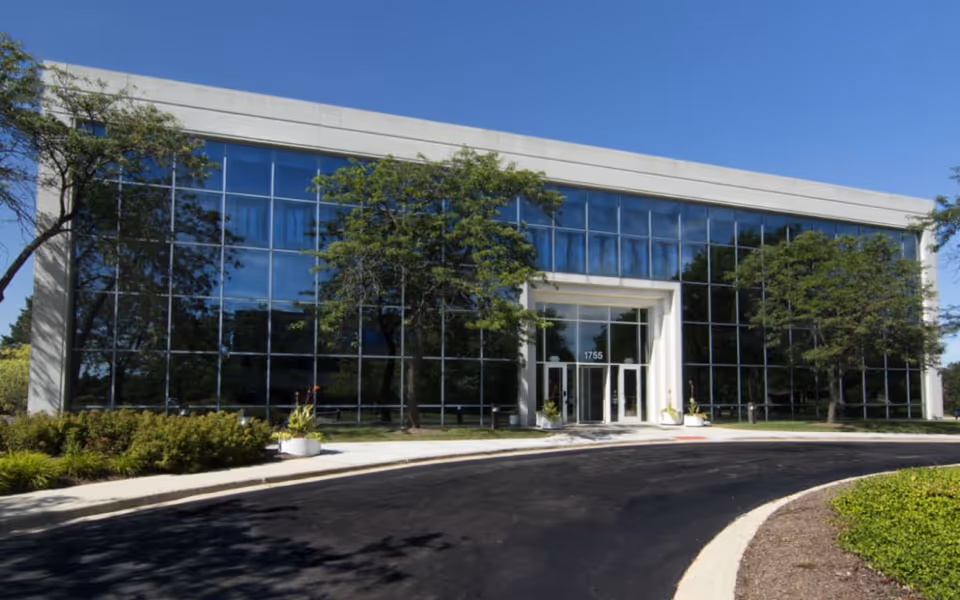 A modern glass-front senior living facility entrance with trees and a curved driveway.