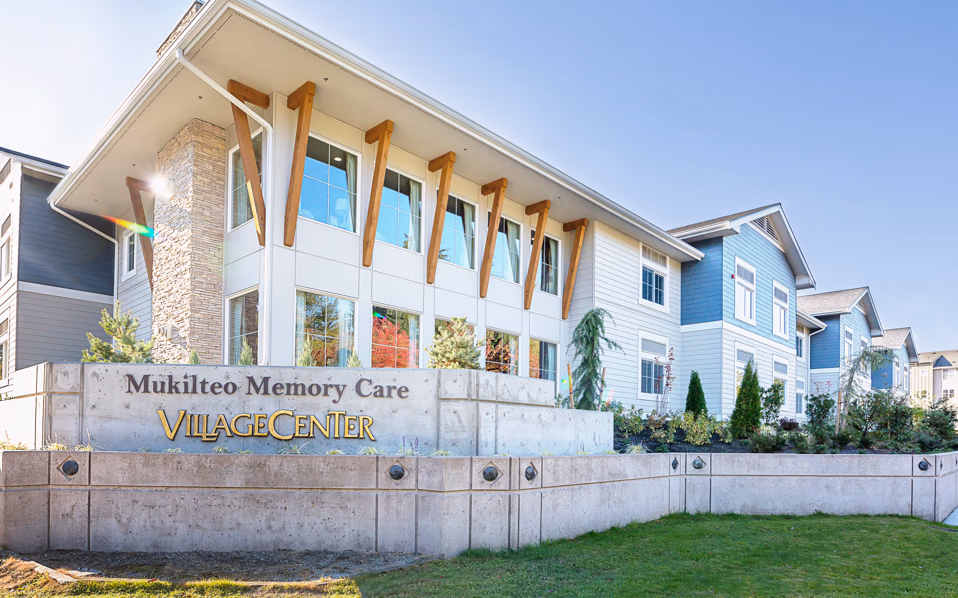 Front exterior of the Mukilteo Memory Care VillageCenter building with a prominent entrance sign and landscaped grounds.
