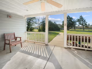 Covered porch with bench, ceiling fan, and view of green lawn and path.