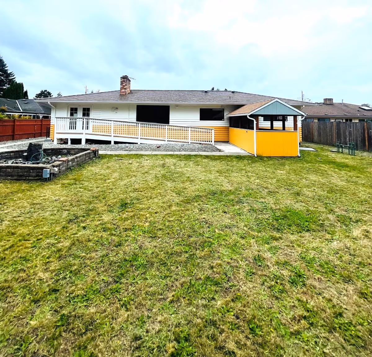 Single-story house with white siding, yellow accents, a ramp, and a large grassy yard.