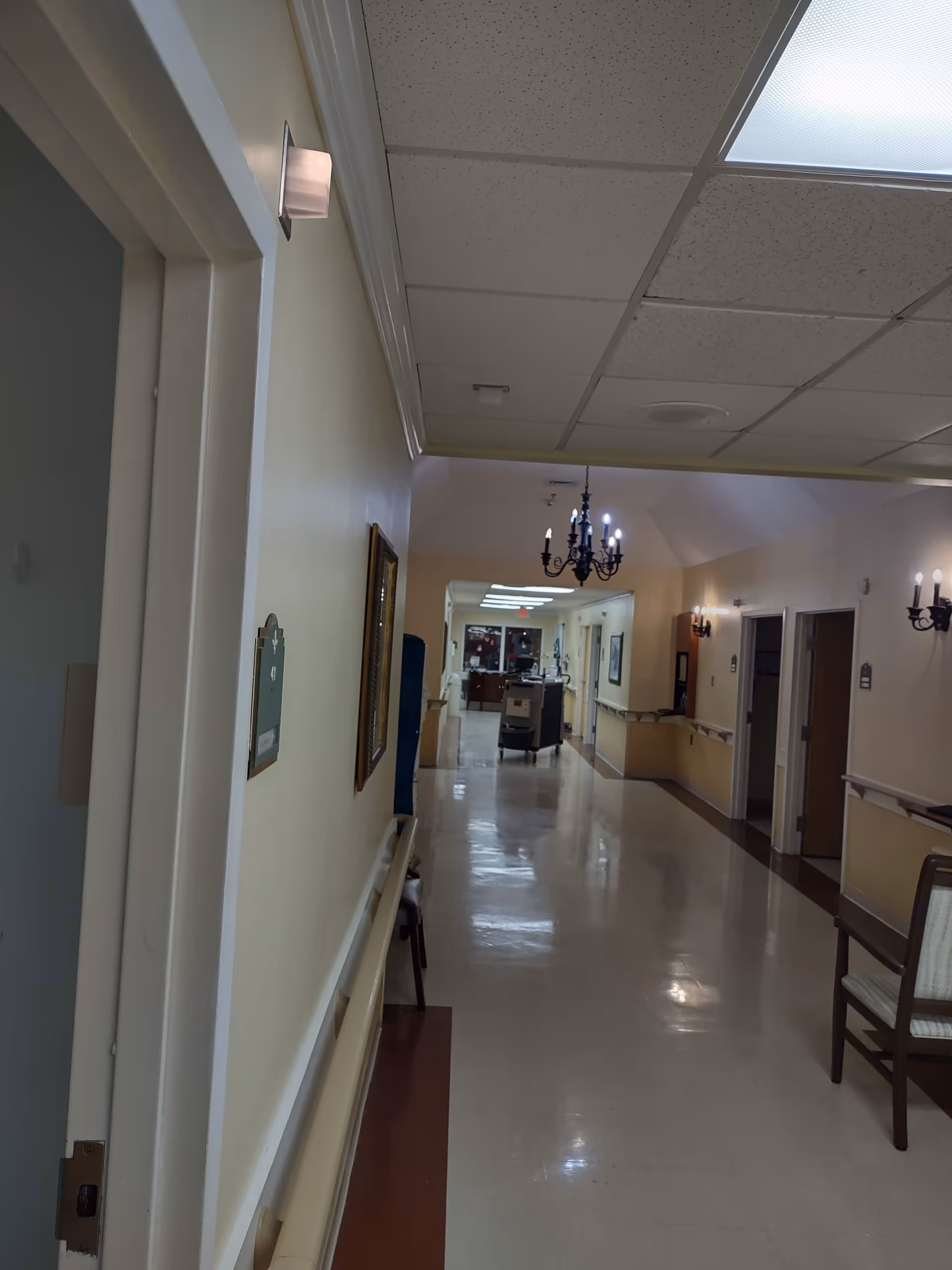 Interior hallway of a senior living center with chandeliers and handrails.