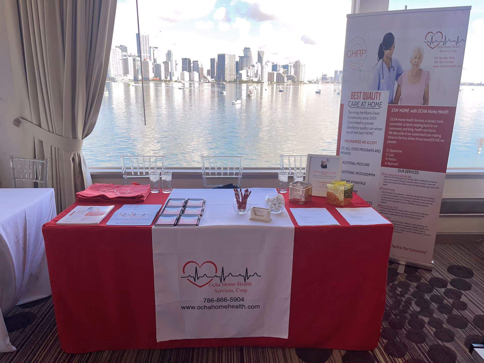 Indoor conference table with red cloth, brochures, and a tall banner overlooking water.